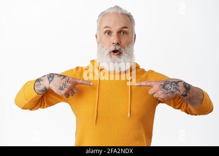 Überrascht reifer bärtiger Kerl mit Tätowierungen, die auf sich zeigen, in Unglauben erstaunt keuchen, ausgewählt werden, Arbeit bekommen, in Ehrfurcht schauen, über Weiß stehen Stockfoto