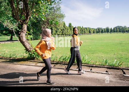 Zwei asiatische Mädchen in Kopftüchern joggen gemeinsam und plaudern Am Nachmittag Stockfoto