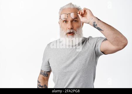 Überrascht reifer Kerl mit langem Bart, Take-off-Brille und Blick in Ehrfurcht, starrte auf etwas erstaunliches, stehend in grauen T-Shirt gegen weiß Stockfoto