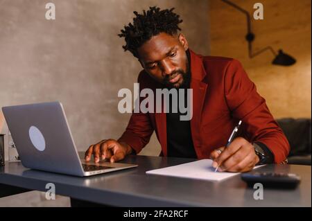 Schwarzer Geschäftsmann, der am Laptop arbeitet und sich Notizen machen kann Stockfoto