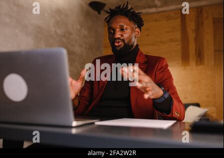 Ein fokussierter schwarzer Mann in einem Anzug arbeitet an einem Laptop. Telearbeit von zu Hause aus Stockfoto