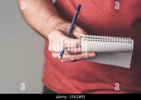 Nahaufnahme einer Person, die einen kleinen spiralförmigen Notizblock mit Bleistift hält Eine Hand Stockfoto