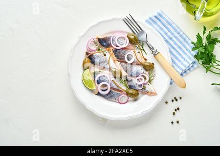 Gesalzener Hering mit Gewürzen, Kräutern und Zwiebeln auf weißem Teller auf hellem Steingrund mit Kopierfläche. Marinierter Fisch in Scheiben. Essen mit gesunder ungesättigter Nahrung Stockfoto