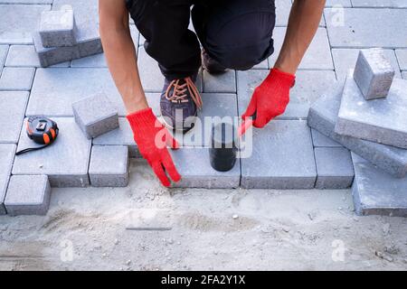 Der Meister in gelben Handschuhen legt Pflastersteine Stockfoto