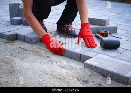 Der Meister in gelben Handschuhen legt Pflastersteine Stockfoto