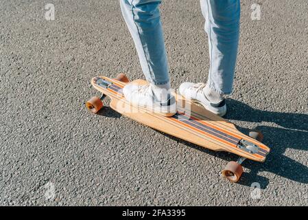 Nahaufnahme Nehmen Sie die Füße eines nicht erkennbaren Mannes auf einem Skateboard auf dem Straßenasphalt auf. Er projiziert einen harten Schatten auf den Asphalt. Stockfoto