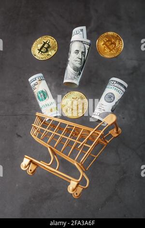 Dollarscheine und itkon-Münzen flogen vor dunklem Hintergrund aus dem Goldenen Korb. Geschäftskonzept, Finanzwesen, Handel oder Börseninvestitionen Stockfoto