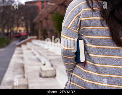 Rückansicht einer Frau, die mit einem Buch unter ihrem Arm im Freien läuft. Mit Kopierplatz für Text. Stockfoto