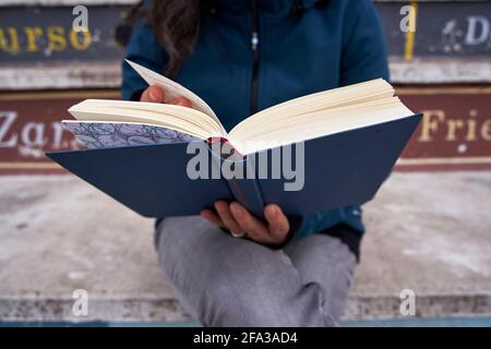 Detail eines offenen Buches, das von einer Frau gehalten wird, abgeschnitten aus dem Fokus. Stockfoto