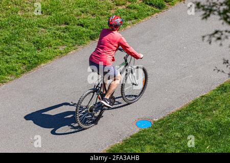 Ältere Frau, die auf einem gepflasterten Weg mit dem Fahrrad unterwegs ist Steveston British Columbia, Kanada Stockfoto