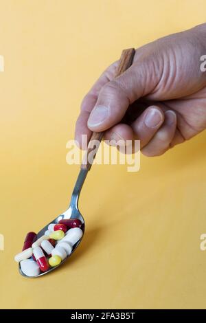 Vorderansicht einer Hand mit einem Löffel voller Vitamin- und Mineralpillen isoliert auf einem gelben Hintergrund, Nahrungsergänzungsmittel Gesundheitsprodukt. Stockfoto