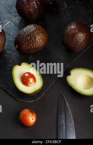 Reife Avocados in einem Korb auf einem schwarzen Tisch, mit einer geschnittenen Frucht und einem Stein. Freier Speicherplatz, Draufsicht Stockfoto