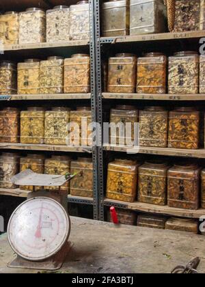 Eine alte, analoge Waage vor Regalen, Regale mit getrockneten Blättern, Kräutern, Gewürzen in Plastikgläsern. In der alten Spice Alley in Taipei, Taiwan. Stockfoto