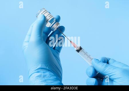 Nahaufnahme der Hände eines Arztes mit blauen Handschuhen zur Vorbereitung des Spritze zur Impfung auf blauem Hintergrund Stockfoto
