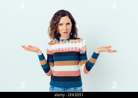 Junge beiläufige Frau im Unglauben zuckt Schultern mit verwirrtem Ausdruck, während sie vor weißem Hintergrund steht. Stockfoto