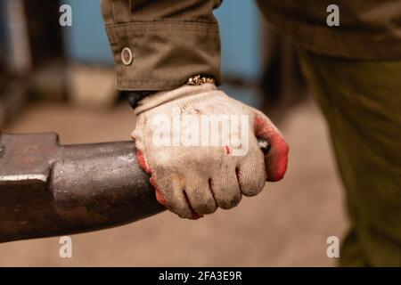 Traditionelle Metallbearbeitung in einer Schmiede. Eine Hand, die einen Arbeitshandschuh trägt, ruht aus nächster Nähe auf einem Amboss. Stockfoto