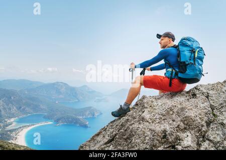 Der junge Backpacker sitzt auf einer Klippe und genießt die Bucht am Mittelmeer während des Lykischen Wanderwegs. Berühmte Likya Yolu türkische Route. Acti Stockfoto