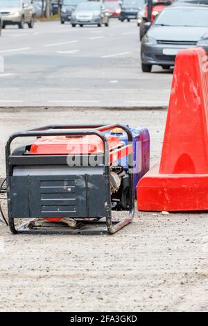 Ein elektrischer Generator und ein Benzinkanister auf einem eingezäunten Arbeitsbereich einer Straße, die repariert wird. Vertikales Bild, Kopierbereich. Stockfoto