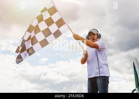 Mann winkt eine karierte Flagge an der Ziellinie von Das Rennen Stockfoto