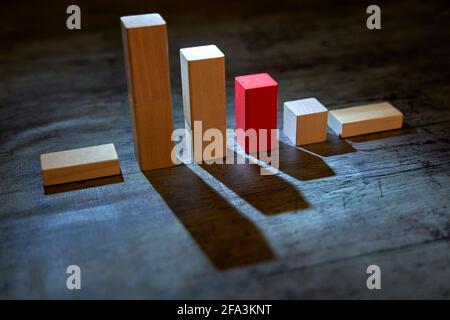 Satz von Holzblöcken in Form eines Verlustgraphen mit einem roten Block, der die Abnahme anzeigt. Low-Key-Fotografie mit harten Schatten. Konzept des Niedergangs, de Stockfoto