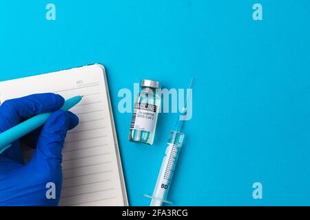 Impfhintergrund mit Arzthand, Impffläschchen und Spritze auf blauem Hintergrund, Draufsicht Foto Stockfoto