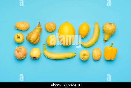 Flach mit verschiedenen gelben Früchten und Gemüse auf einem blauen Tisch legen. Frisches Gemüse und Obst symmetrisch auf farbigem Hintergrund angeordnet Stockfoto