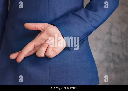 Mann in blauem Business-Anzug mit gekreuzten Fingern hinter dem Rücken. Grauer Hintergrund Stockfoto