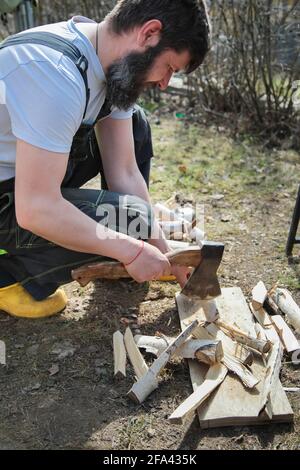 Ein bärtiger Mann in Overalls hackt Holz für ein Feuer. Birkenzweige. Nahaufnahme. Stockfoto