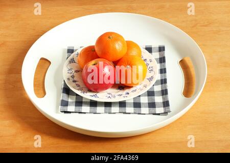 Weißes Kunststofftablett mit Äpfeln und Mandarinen in einem Teller auf einem Holztisch. Nahaufnahme Stockfoto