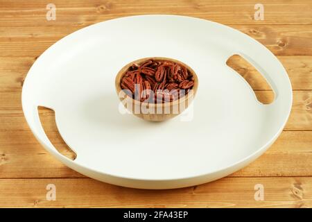 Weißes Kunststofftablett mit Pekannüssen in einer Bambusschüssel auf einem Holztisch. Nahaufnahme. Tageslicht Stockfoto