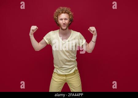 Junger Mann in gelben Kleidern posiert isoliert auf rotem Wandhintergrund, Studioportrait. Menschen Emotionen Lifestyle-Konzept. Erstellen Sie ein Modell für den Kopierbereich. Steigt Stockfoto