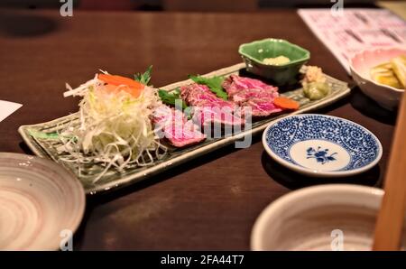In dünne Scheiben geschnittenes, seltenes Yamagata-Rindfleisch-Tataki mit einem kleinen Salat serviert Auf einem langen Zierteller Stockfoto