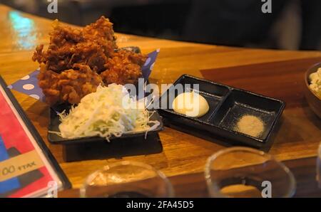 Ein kleiner Teller mit japanischem „Karaage“ (Eine Art gebratenes Huhn) Und Beilagensalat mit Mayonnaise und weißem Pfeffer serviert Eine Holztheke Stockfoto