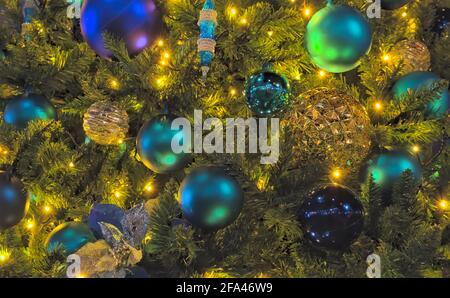 Nahaufnahme einer Reihe von blauen und goldenen Ornamenten auf einem Weihnachtsbaum, beleuchtet von gelben Weihnachtslichtern Stockfoto