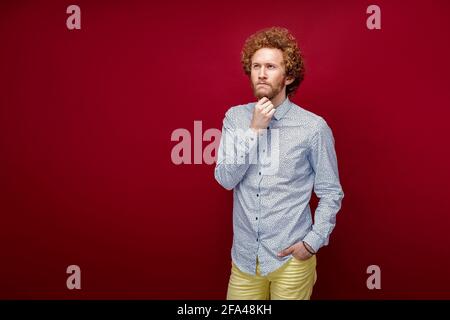 Junger gutaussehender Mann im Urlaub trägt Sommerhemd auf isoliertem rotem Hintergrund mit Hand auf Kinn und denkt über Frage, nachdenklichen Ausdruck Stockfoto
