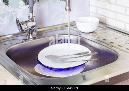 Metallwaschbecken in der Küche voller schmutziger Geschirrstapel. Hausarbeit, Geschirr waschen, Haushaltsaufgaben Konzept. Stockfoto