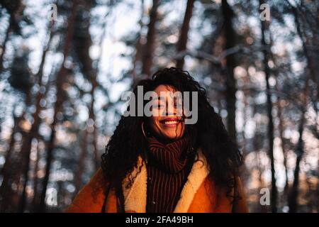 Porträt einer glücklichen jungen Frau, die im Winter im Wald steht Stockfoto