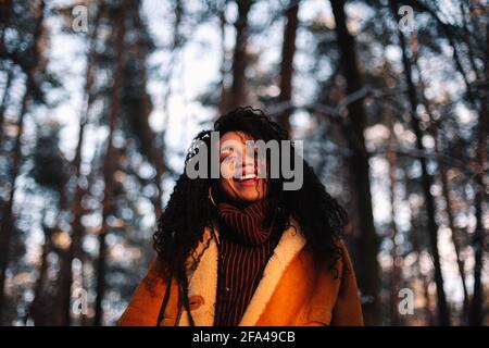 Porträt einer glücklichen jungen Frau, die im Winter im Wald steht Stockfoto