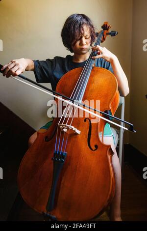 Nahaufnahme eines Jungen mit intensivem Fokus, der Cello spielt Ein Treppenhaus Stockfoto