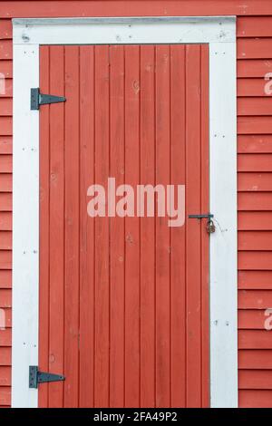 Ein großer alter roter Holzschuppen oder eine Scheunentür mit weißen Zierleisten an einem Ausbissgebäude mit großen Scharnieren. Stockfoto