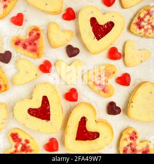 Herzförmige Kekse mit roter Marmelade und Bonbons flach legen Auf Marmortisch Stockfoto