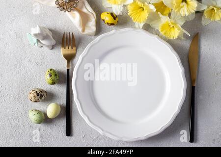 Ostertisch mit Narzissen, Wachteleiern und Hase auf hellgrauem Tisch. Elegantes Abendessen. Platz für Text. Blick von oben. Stockfoto