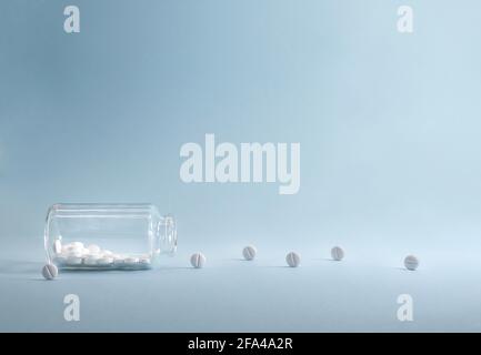 Durchsichtiges Glas mit weißen Tabletten, die aus ihm herausrollten. Auf blauem Hintergrund. Stockfoto