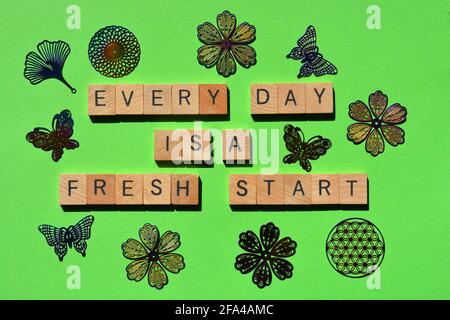 „Every Day is a Fresh Start“, Wörter in Holzbuchstaben, umgeben von zufälliger Blumen- und Schmetterlingsform, isoliert auf Grün Stockfoto