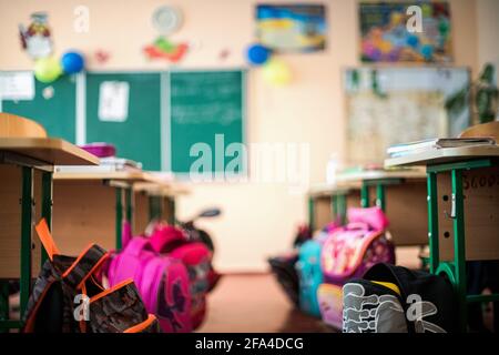 Rucksäcke in der Nähe von Schreibtischen in einem leeren Klassenzimmer ohne Kinder und Lehrer in der Grundschule. Bildungskonzept ohne Studenten aufgrund des Corona-Virus COVI Stockfoto