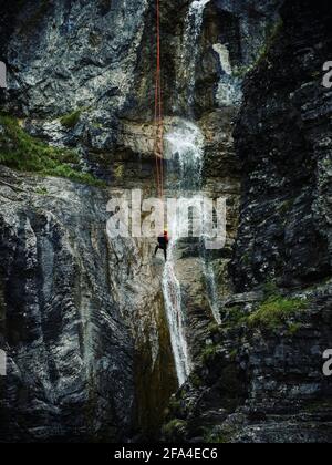 Junger Mann abseilen von vertikalen Felswand Klippe, Abenteuer Sport Spaß Aktivität an Stuibenfaelle Stuiben Wasserfälle in Breitenwang Reutte T Stockfoto