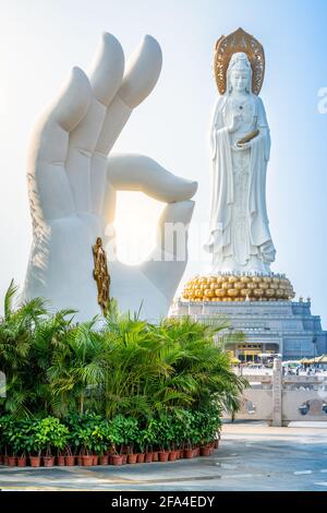 Vertikale Ansicht der weißen Handstatue mit Dharma-Rad und Guanyin der Südsee-Statue im Hintergrund bei Nanshan Buddhismus Kulturpark Tempel in Stockfoto