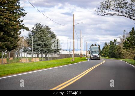 Graues industrielles großes Rig Langstrecken-Semi-Truck, der kommerzielle Fahrzeuge transportiert Fracht in einem trockenen Transporter, der auf dem lokalen Transport unterwegs ist Schmale Straße am Industriebusin Stockfoto