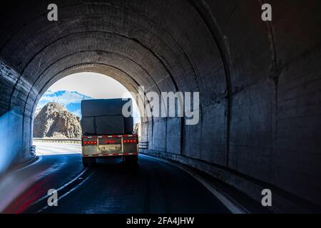 Leistungsstarke klassische große Rig Semi-Truck Transport Flachbett semi Anhänger mit überdachter Holzladung beladen, die die Wicklung eindreht autobahnstraße durch A Stockfoto