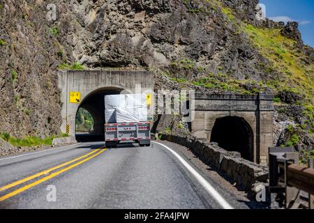 Leistungsstarke klassische große Rig Semi-Truck Transport Flachbett semi Anhänger mit überdachter Holzladung beladen, die die Wicklung eindreht autobahnstraße durch A Stockfoto